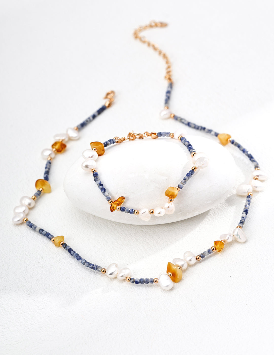Handcrafted jewelry set including a necklace and bracelet with natural pearls, blue spotted stones, and beeswax amber for a unique, earthy aesthetic