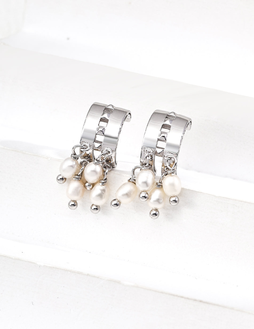 Silver crescent-shaped hoop earrings featuring four dangling natural pearls, sleek and timeless design